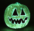 A glowing jack-o’-lantern with triangular eyes and a jagged mouth, lit with a greenish light against a dark background.